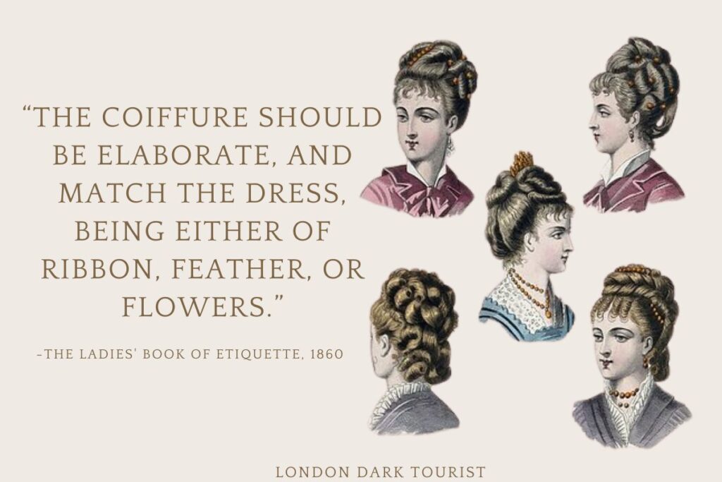 The image is an illustration depicting four Victorian women's hairstyles, showcasing the elaborate and ornate hairdressing of the era. The hairstyles include braids, curls, and buns, often adorned with accessories like ribbons or flowers to complement their attire. Each hairstyle is detailed and sculpted, reflecting the fashion and social standards of the time. A quote from "The Ladies' Book of Etiquette, 1860," emphasizes that the coiffure should be as elaborate as the dress and matched with appropriate accessories, such as ribbons, feathers, or flowers.